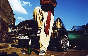 Capa do álbum do Racionais MC's: um homem apoiado num carro com a placa Racionais, de all-star e uma bandana vermelha pendurada na calça