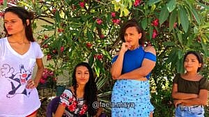 Cena de vídeo do canal de Faela Maya: três mulheres e uma garota debaixo de uma árvore florida na rua, olhando com desprezo e deboche para o canto esquerdo do quadro